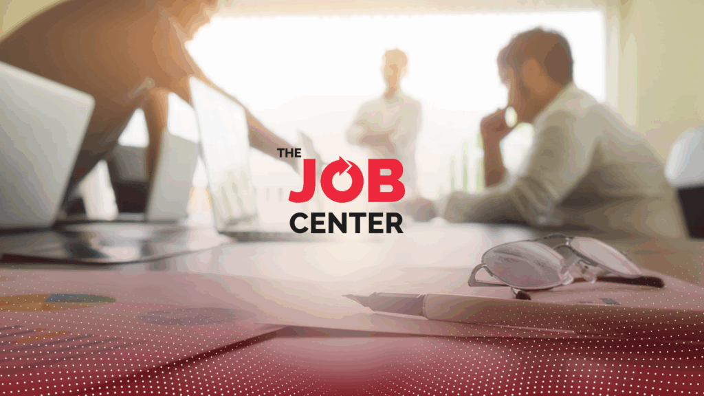 Three men in corporate attire discuss around a conference table with laptops and papers